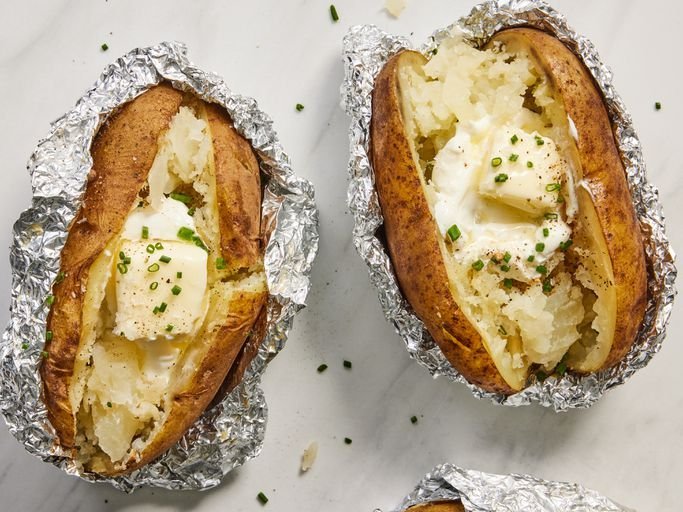 Hands wrapping a large russet potato in aluminum foil for a home meal.