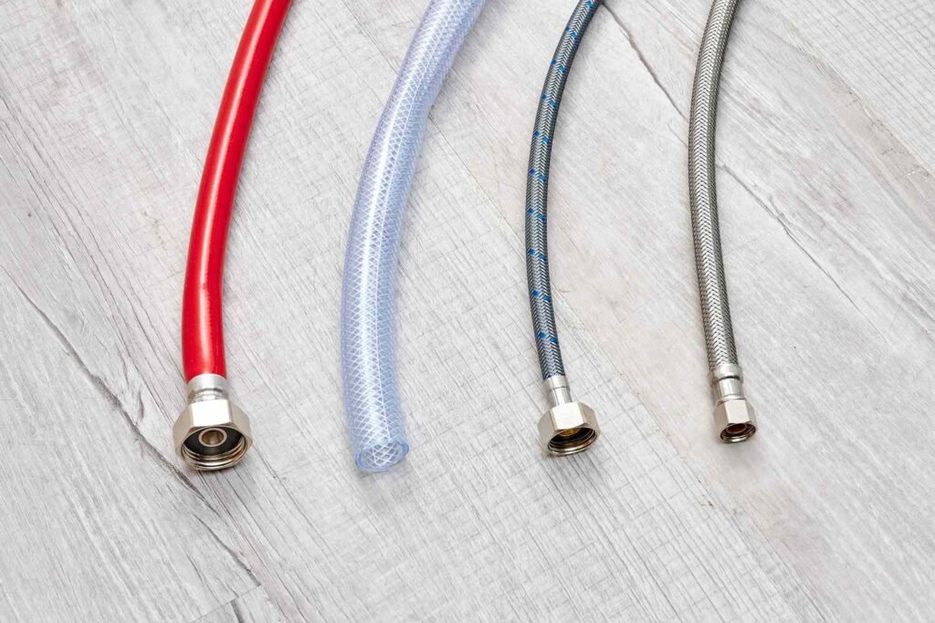 Braided stainless steel and rigid chrome supply lines displayed together on a marble surface.