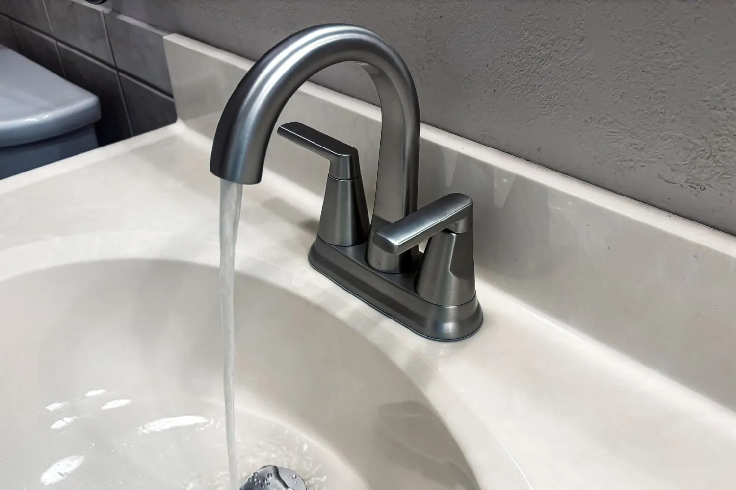 A brushed nickel widespread bathroom faucet installed on a large dark stone vanity.