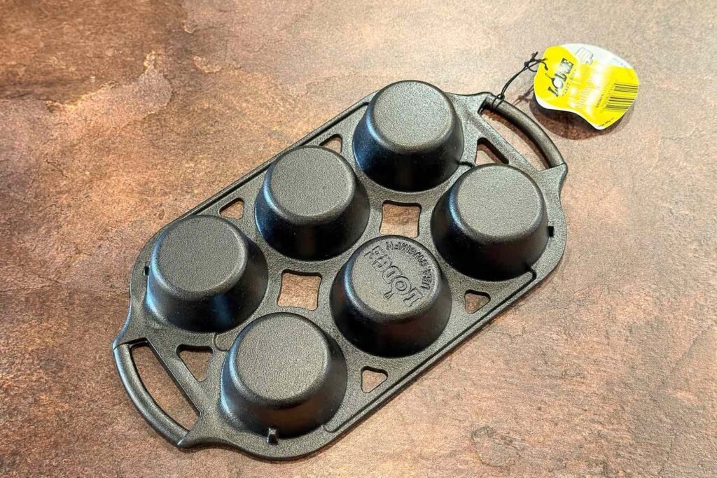 Cast iron muffin pan on oak counter with blueberries and linen towel