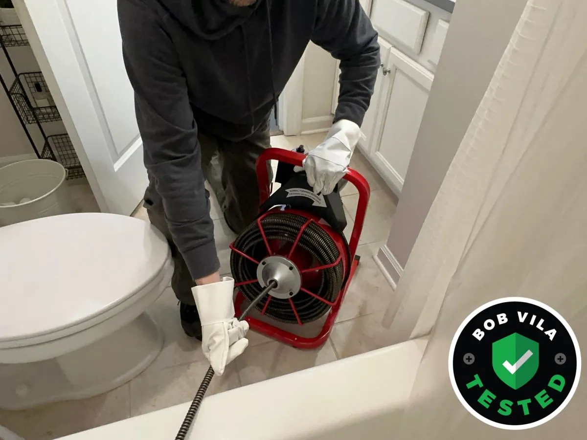 A close-up of a hand auger being inserted into a bathroom sink drain.