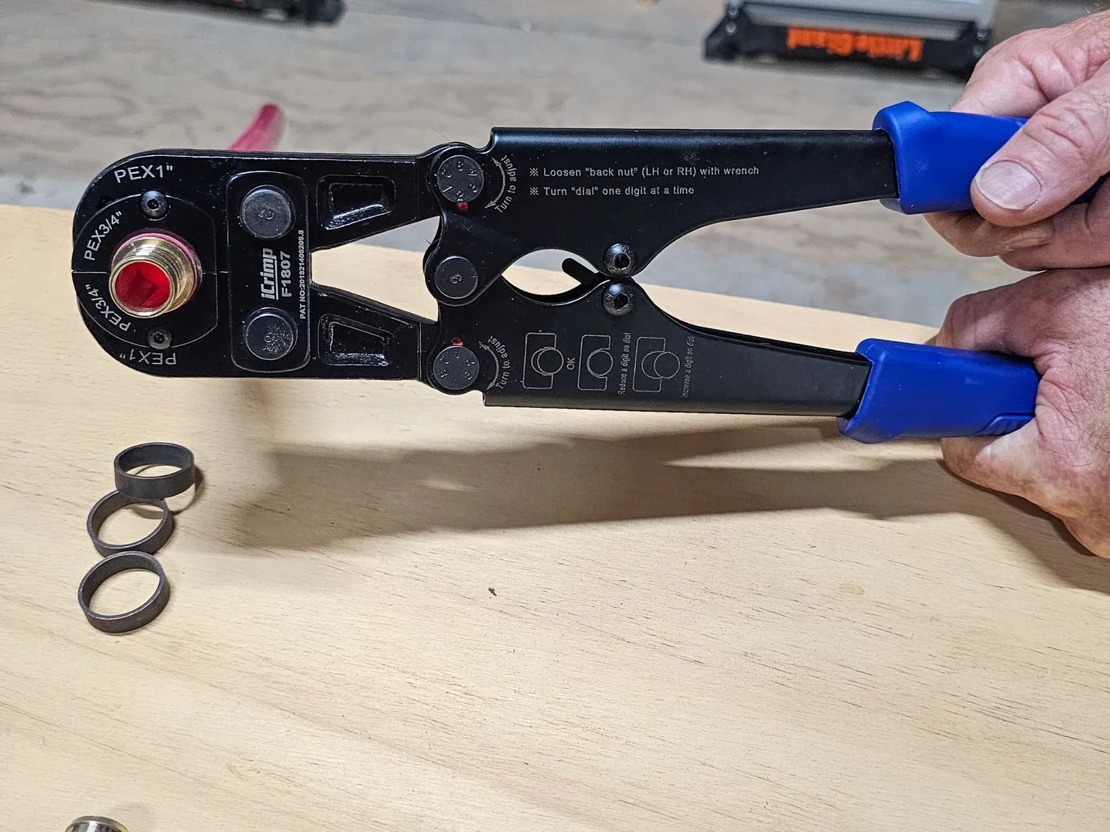 A close-up of a manual PEX crimp tool being used on a pipe connection.