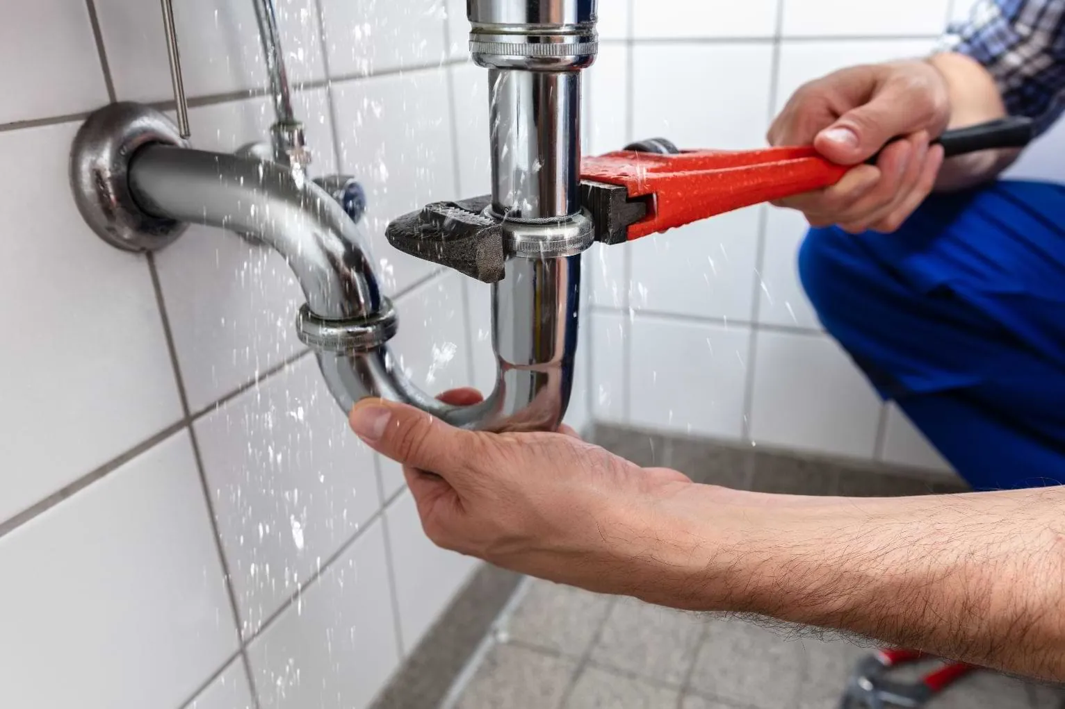 Close-up of plumbing tools being used to tighten a connection under a sink.