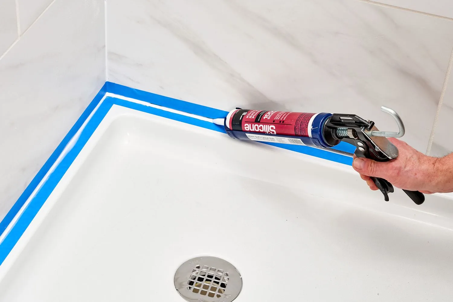 A hand uses a scraper to remove old caulk from a seam.