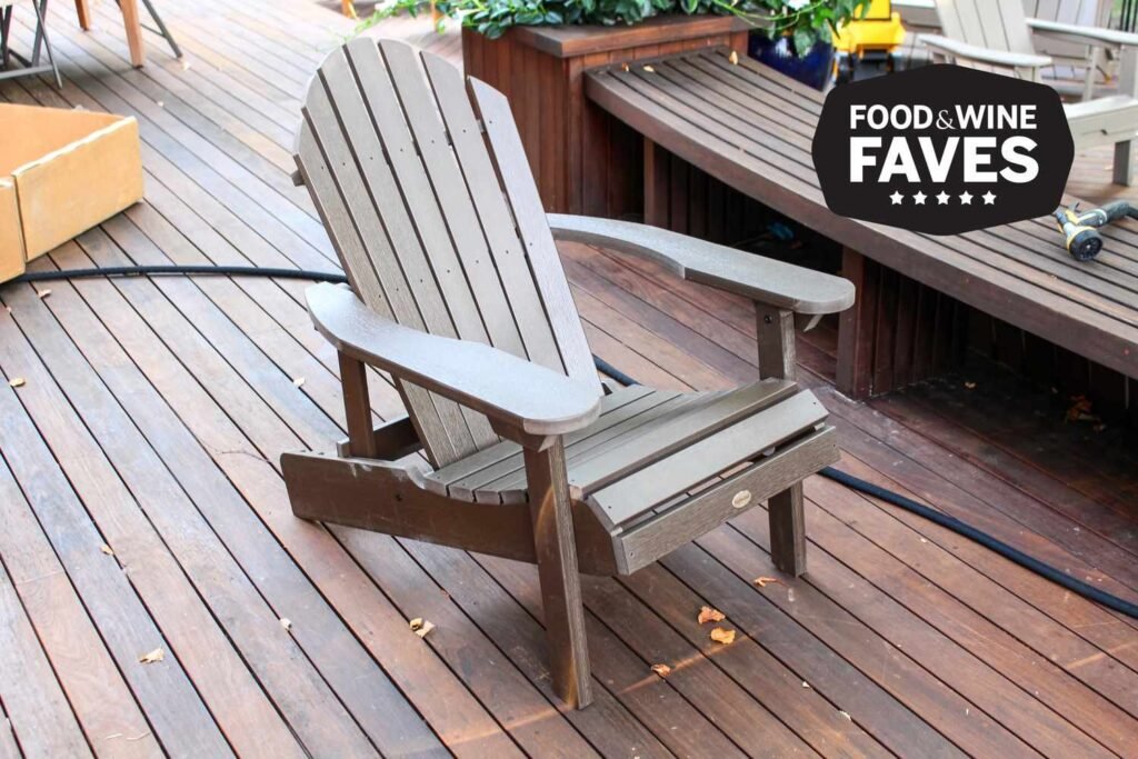 A handcrafted teak wood Adirondack chair sits elegantly on a sunny backyard lawn.