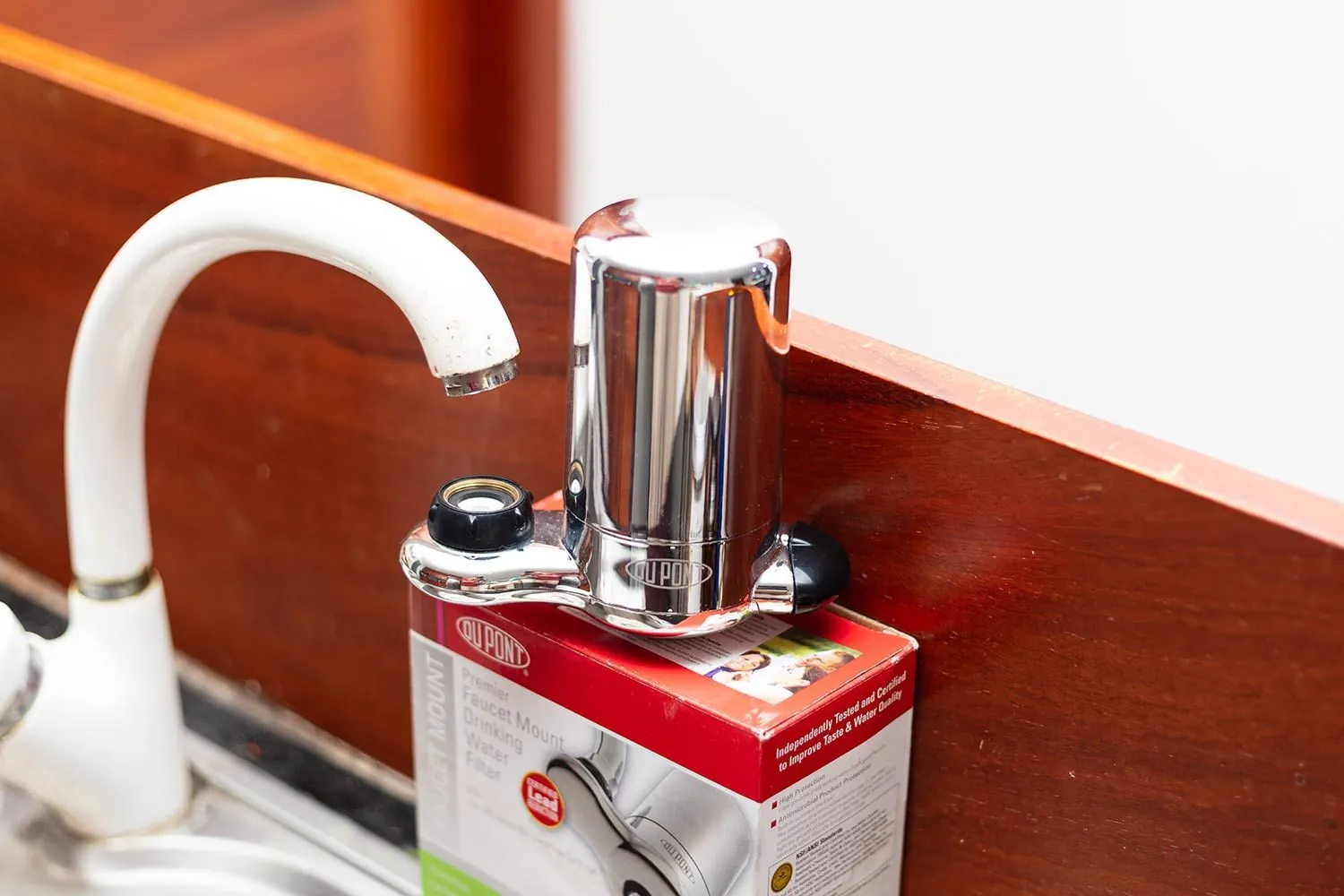 Hands adjusting a faucet mounted water filter in a bright modern kitchen.