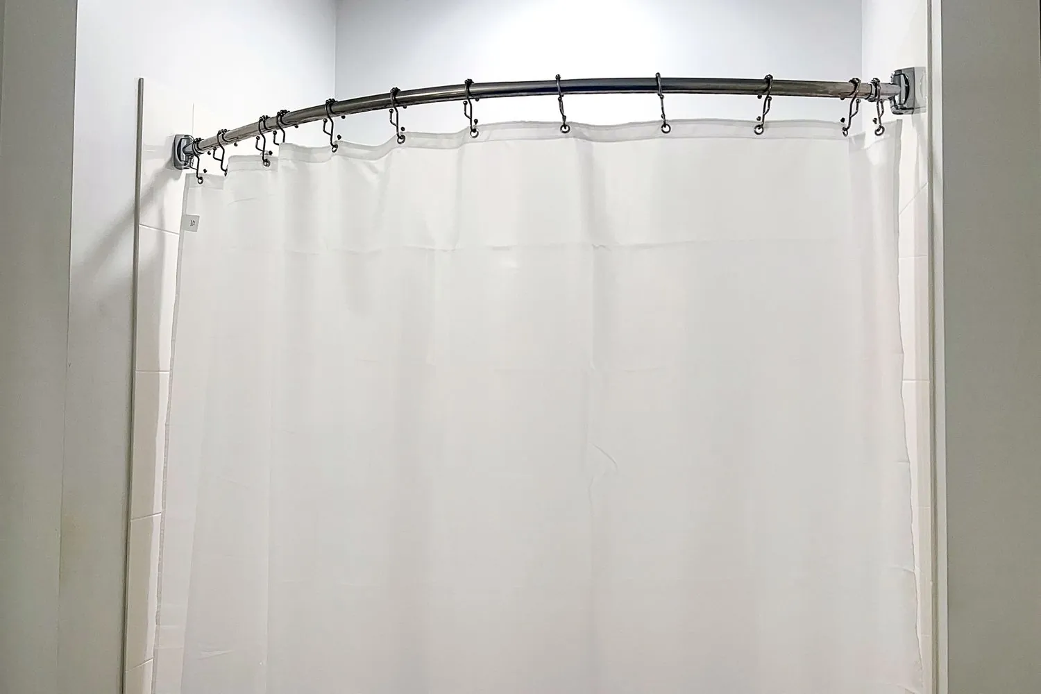 Hands placing a machine-washable polyester shower curtain liner into a laundry machine.