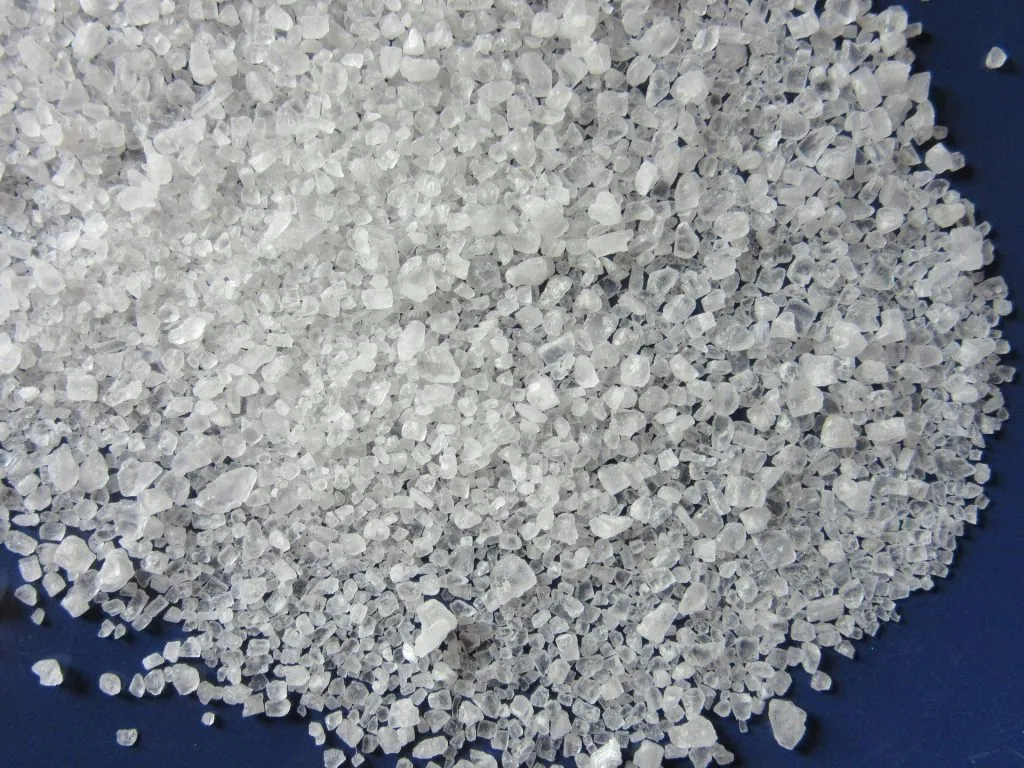 Hands pouring white salt pellets into a home water softener brine tank.