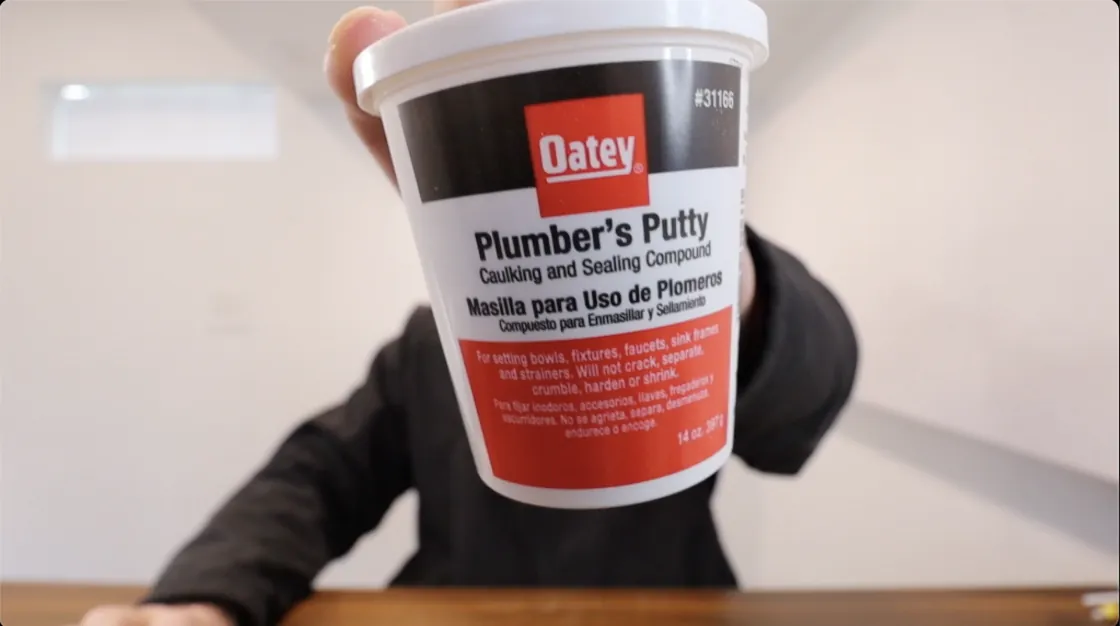 Hands shaping a soft ball of plumbers putty for a kitchen sink drain.