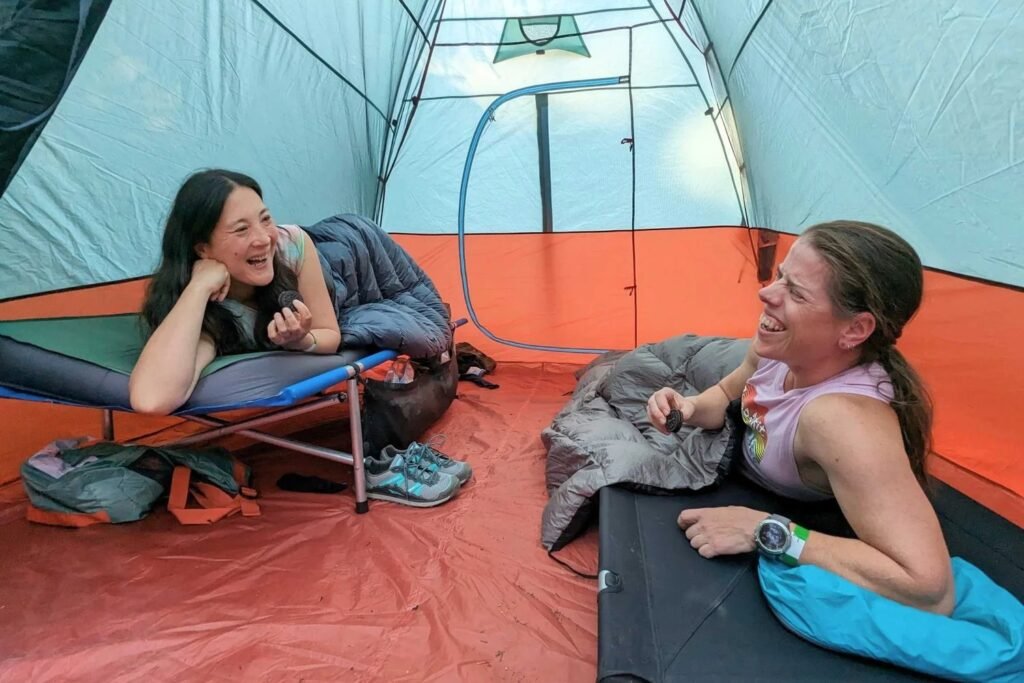 Heavy-duty camping cot on forest ground at dusk with folded blanket and backpack