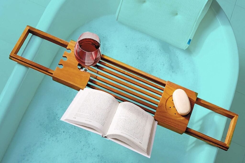 A luxurious bathtub caddy sits across a clean white bathtub in a bright bathroom.