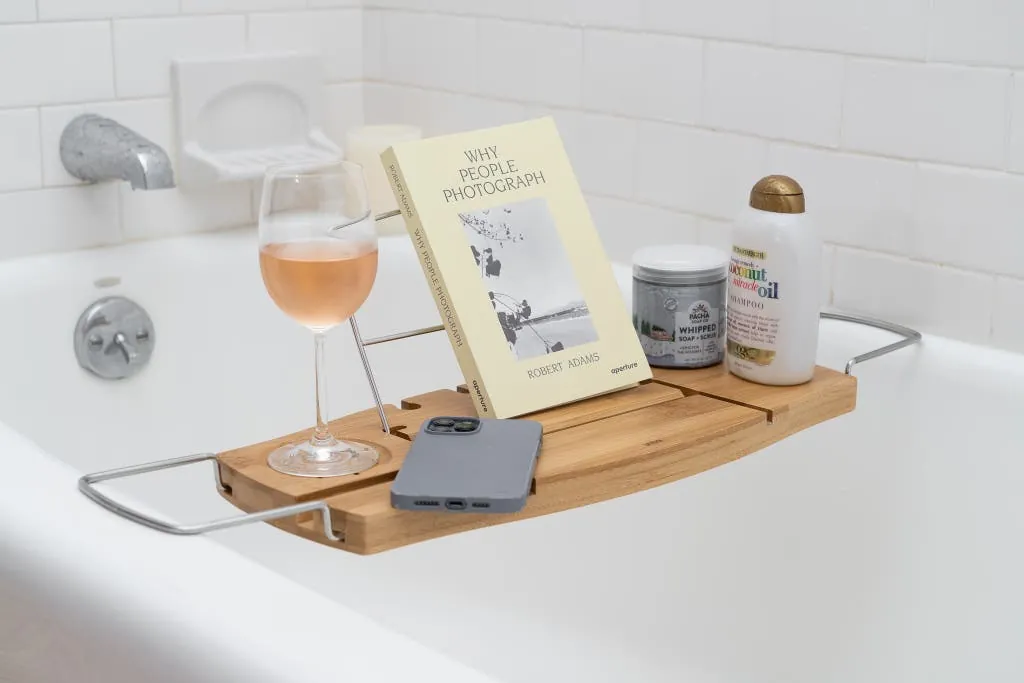 A minimalist clear acrylic bathtub caddy sits on a white tub in a bathroom.