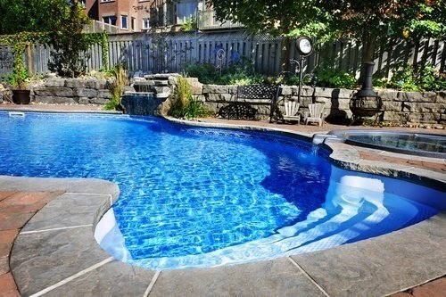 Modern backyard saltwater pool with stone deck and greenery.