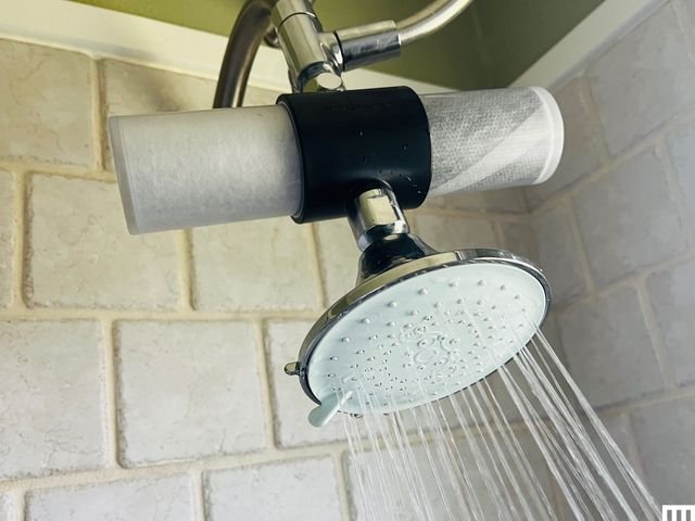 A modern chrome shower head with a filter installed in a bright bathroom.