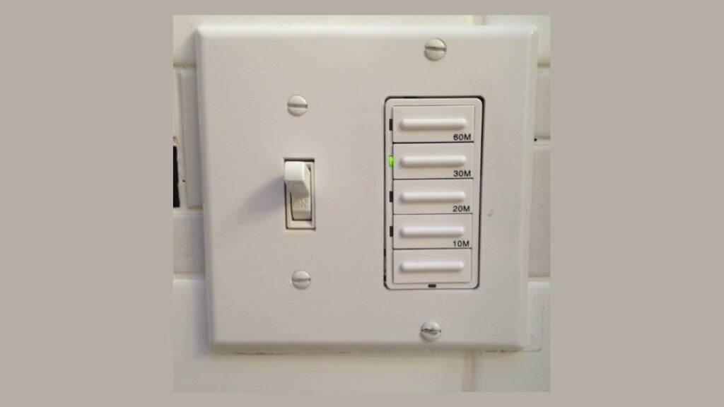 A modern digital bathroom exhaust fan timer switch installed on a tiled wall.