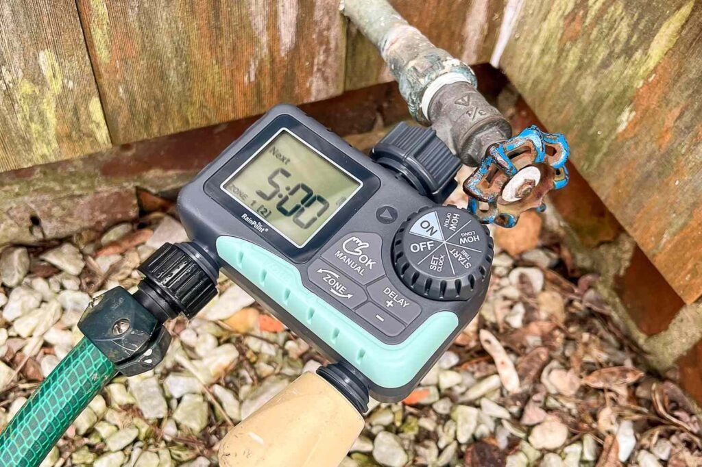 A modern hose bib timer attached to an outdoor faucet in a garden.