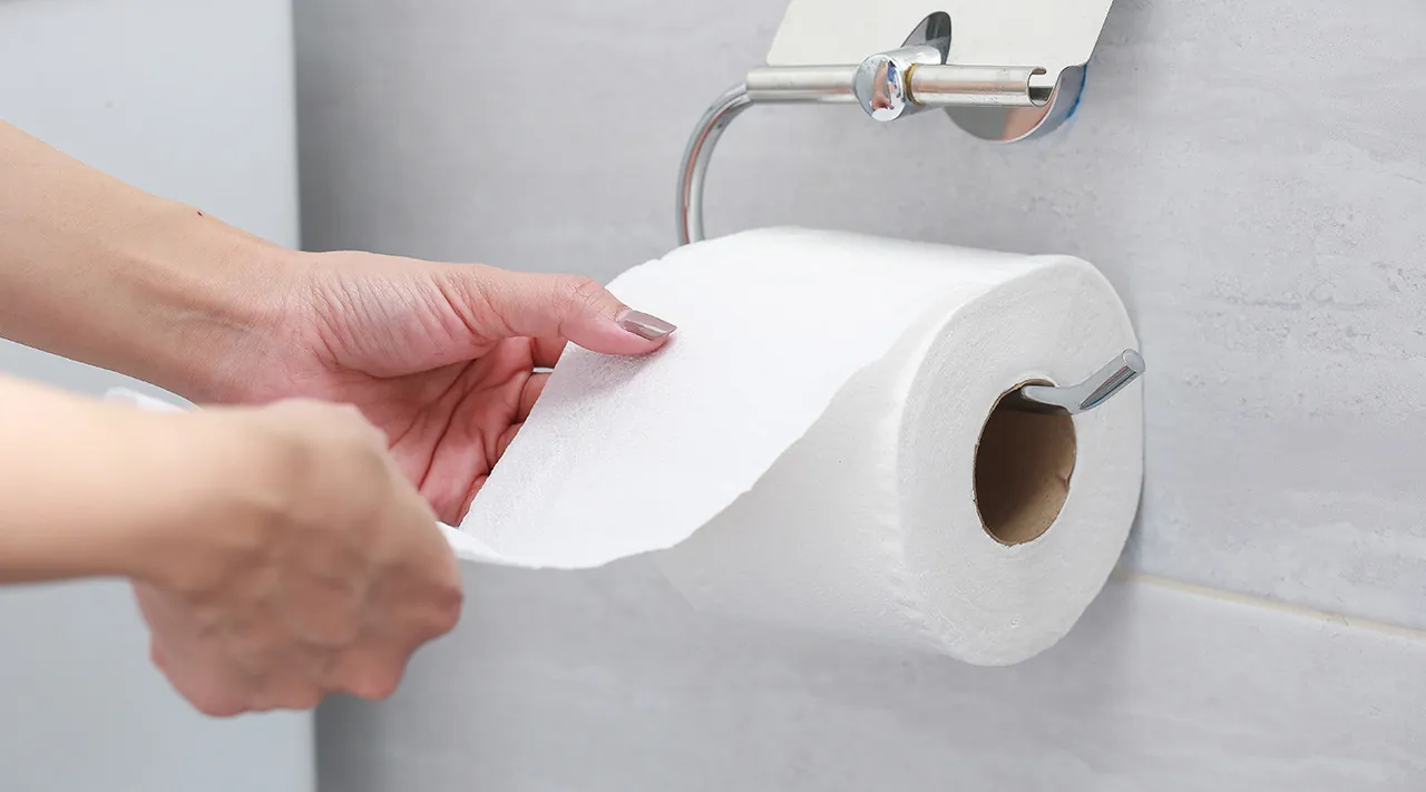 A modern open-arm toilet paper holder installed on a bright subway tile wall.
