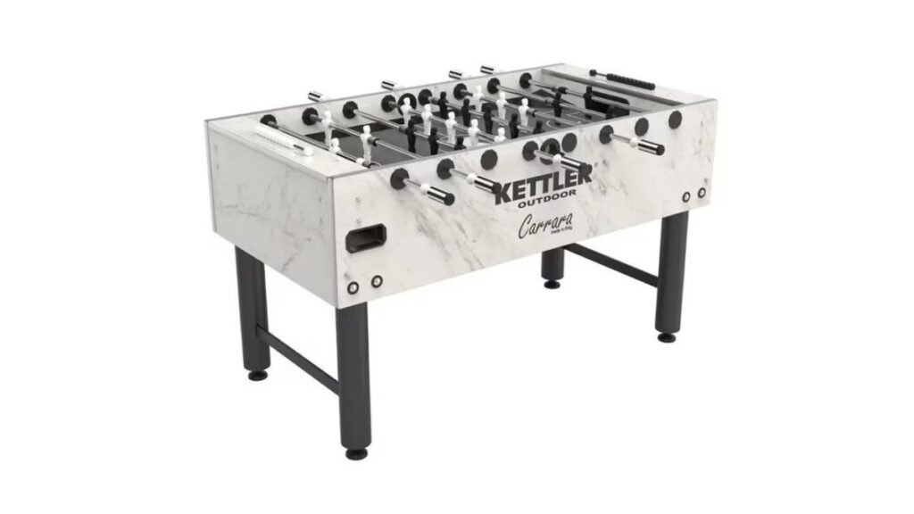 Modern outdoor foosball table on a sunny concrete patio surrounded by greenery.