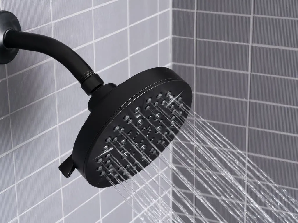 A modern shower head demonstrating a full coverage spray pattern in a bright bathroom.