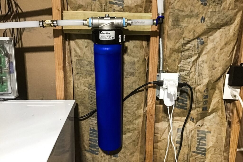 A modern whole house water filtration system installed neatly in a bright residential utility room.