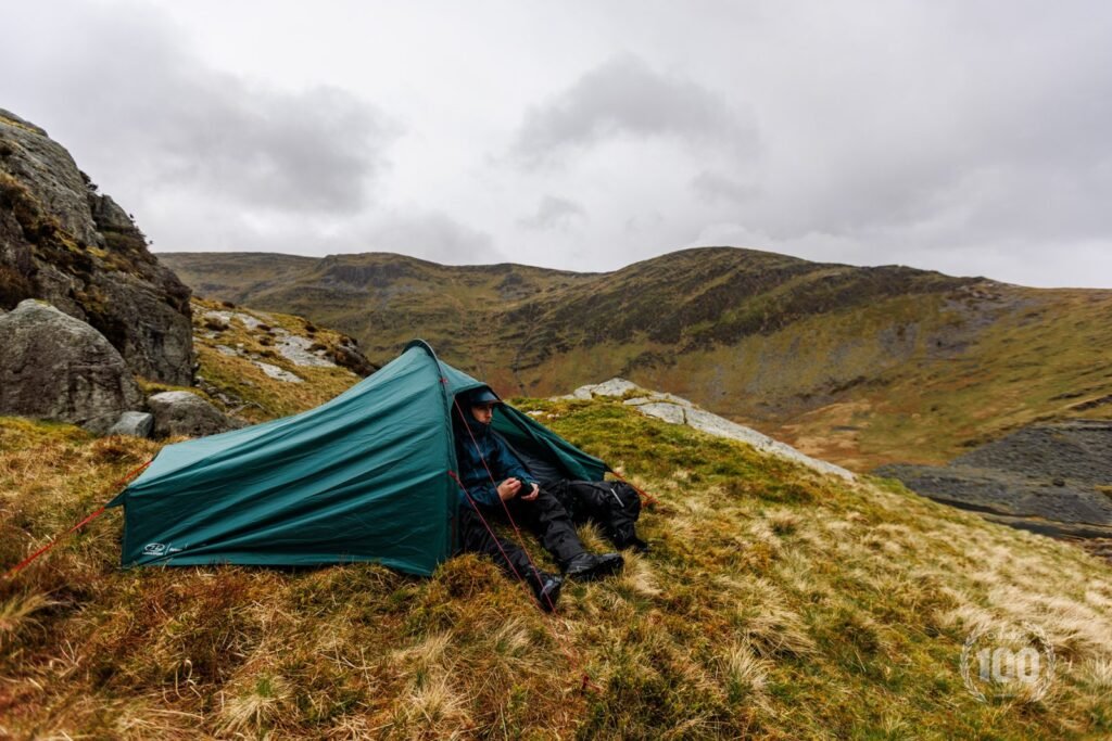 One person tent pitched in a sunny alpine meadow with mountains in the distance