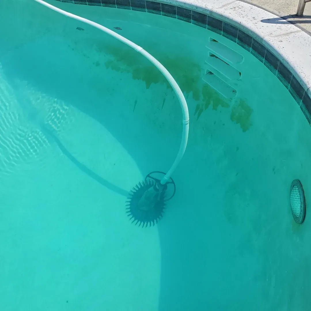 Person brushing yellow residue off pool floor with a long brush.