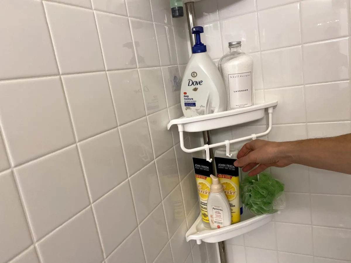 A person checking a smooth bathroom tile surface before installing an adhesive caddy.