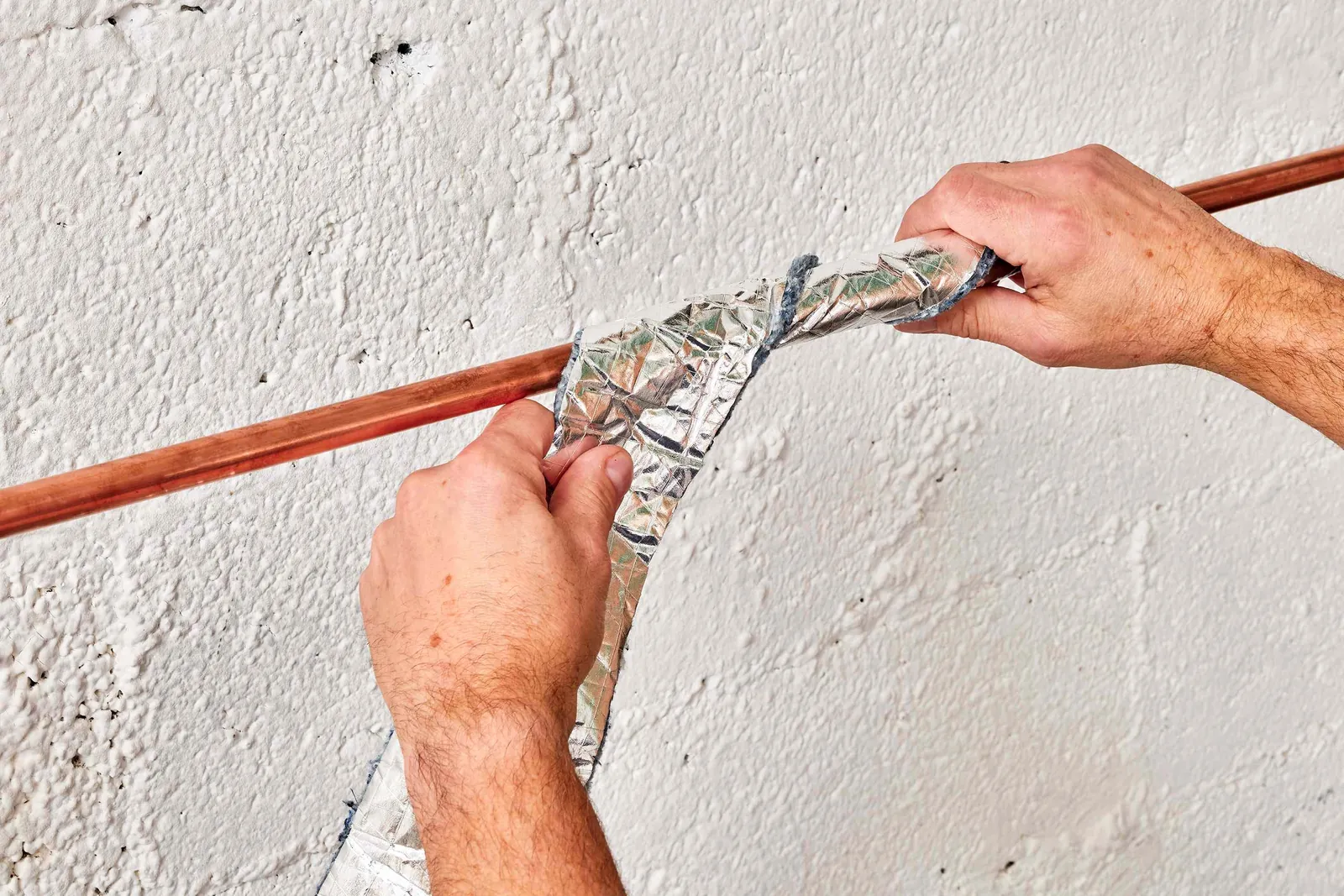 A person installing a grey foam sleeve onto a copper pipe for insulation.