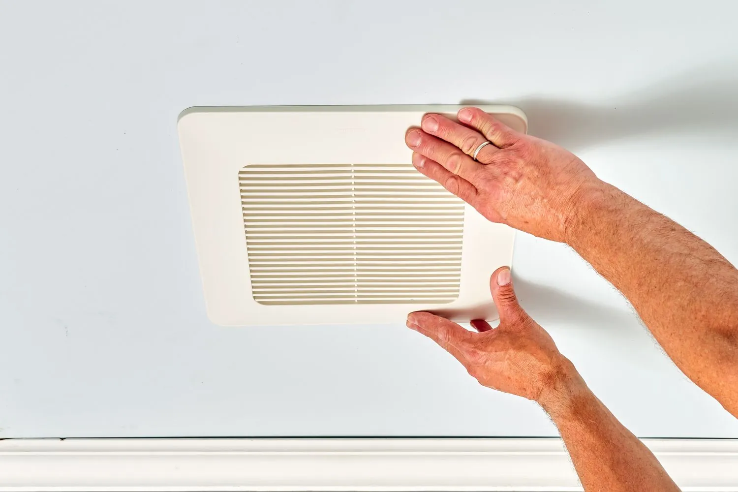 A person measures a bathroom floor to determine the correct exhaust fan size.