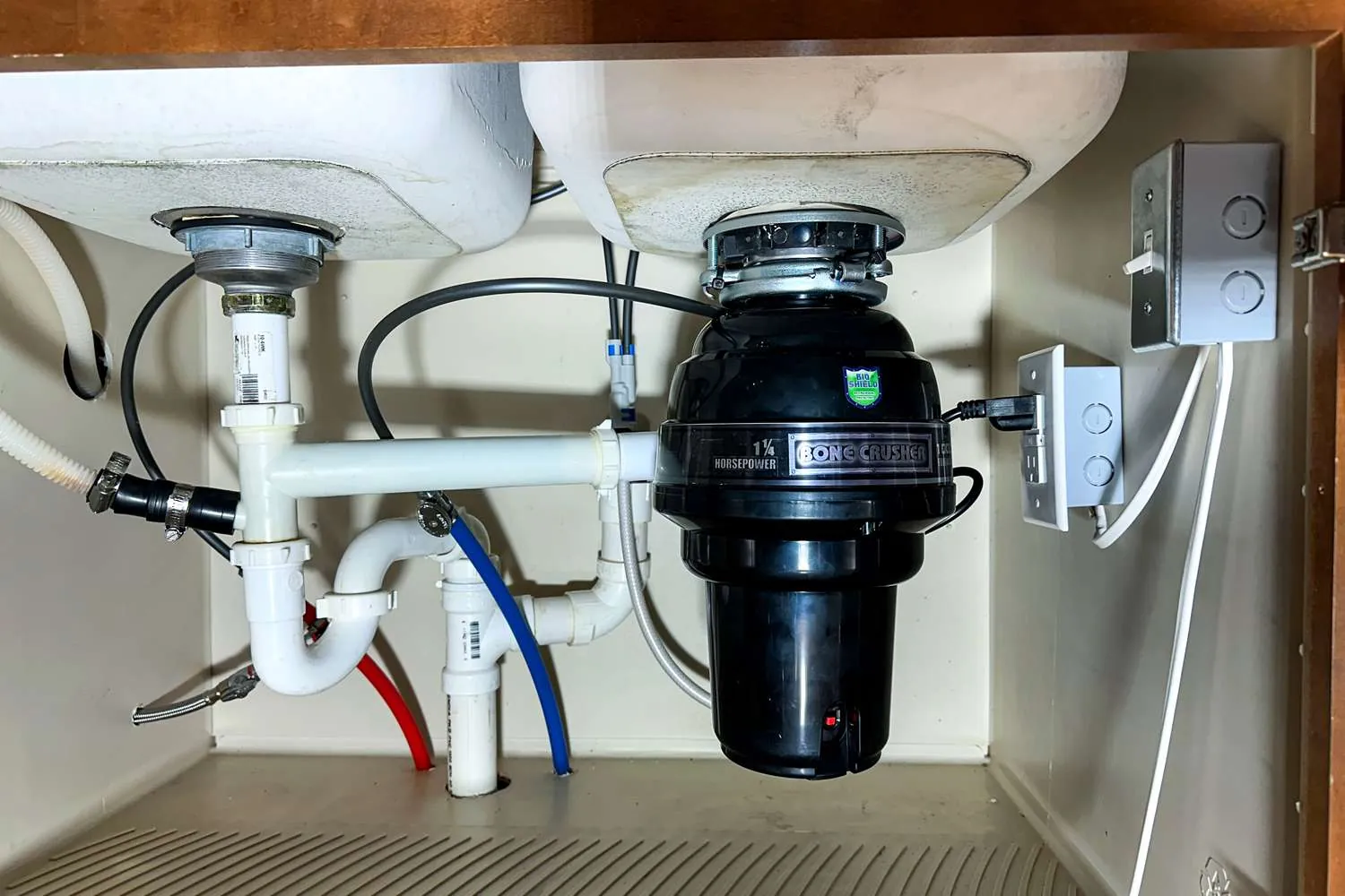 A person measuring the space beneath a kitchen sink to select the right disposal.