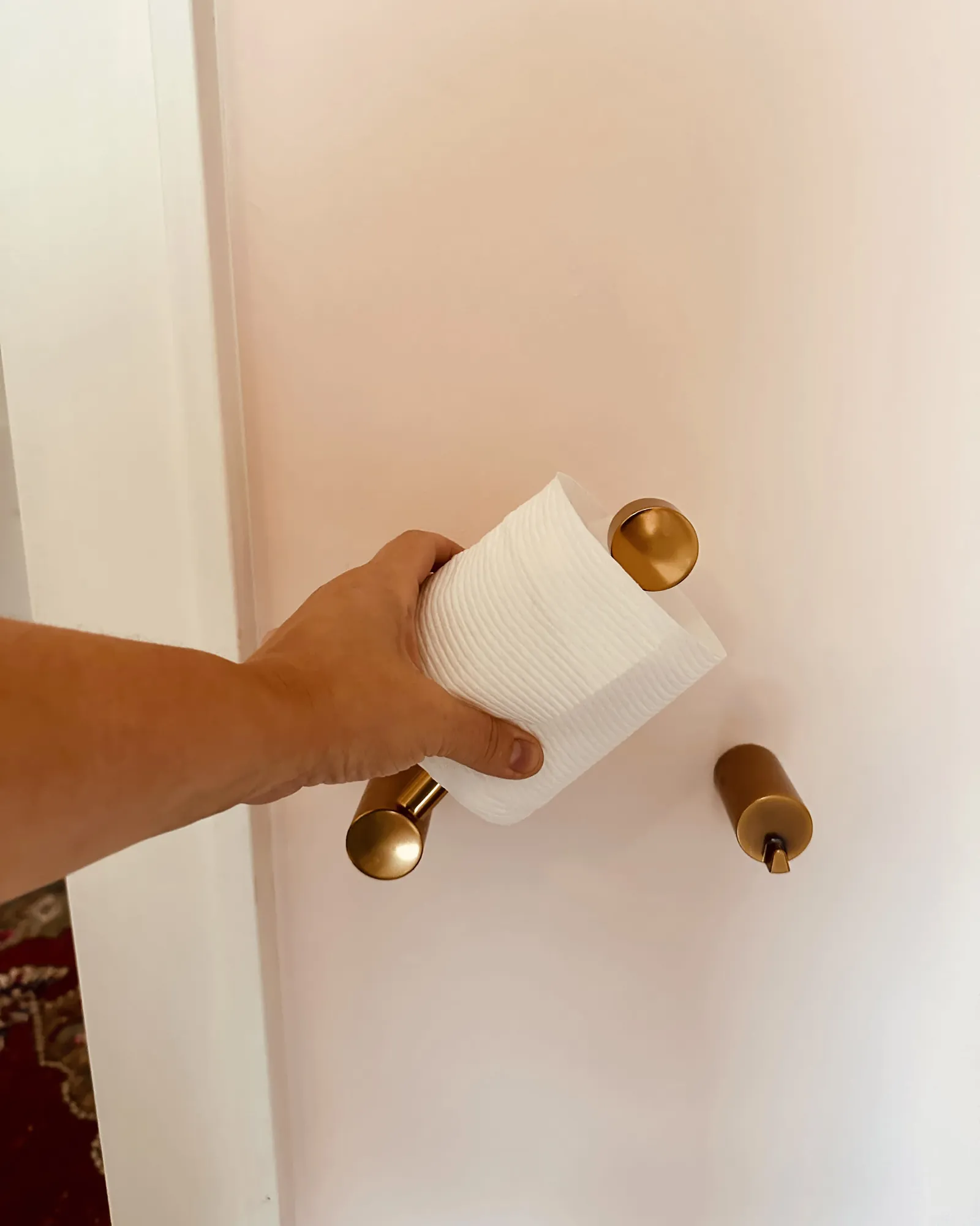 A person repairing a wall-mounted toilet paper holder with a small hand tool.