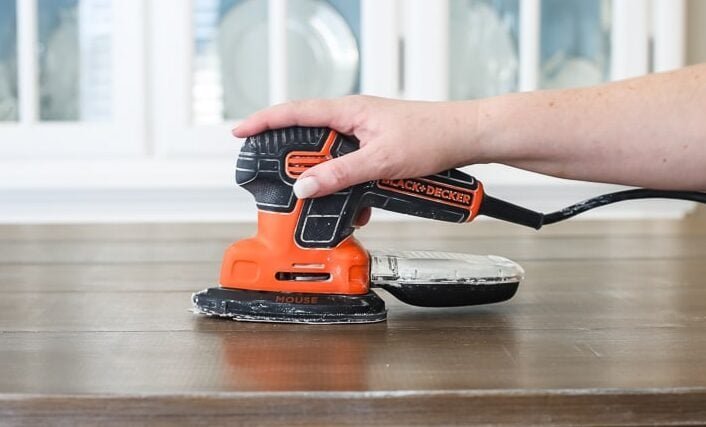A professional detail sander resting on a wooden surface in a bright workshop.