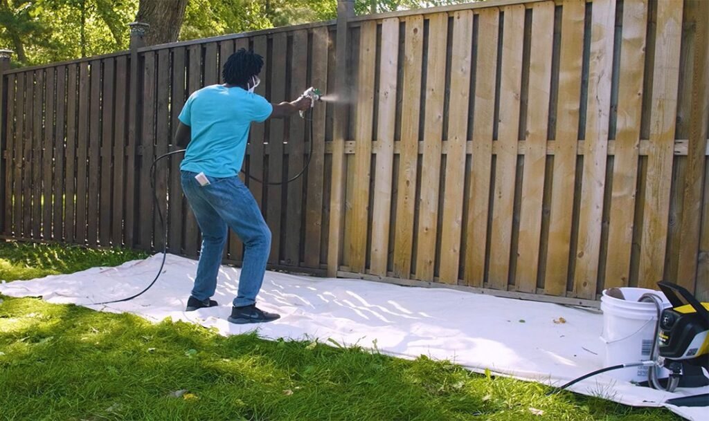A professional paint sprayer sits on a perfectly stained wooden fence in a garden.