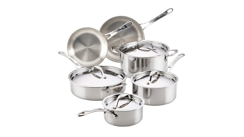 Shiny stainless steel cookware set on a light oak kitchen counter in soft daylight