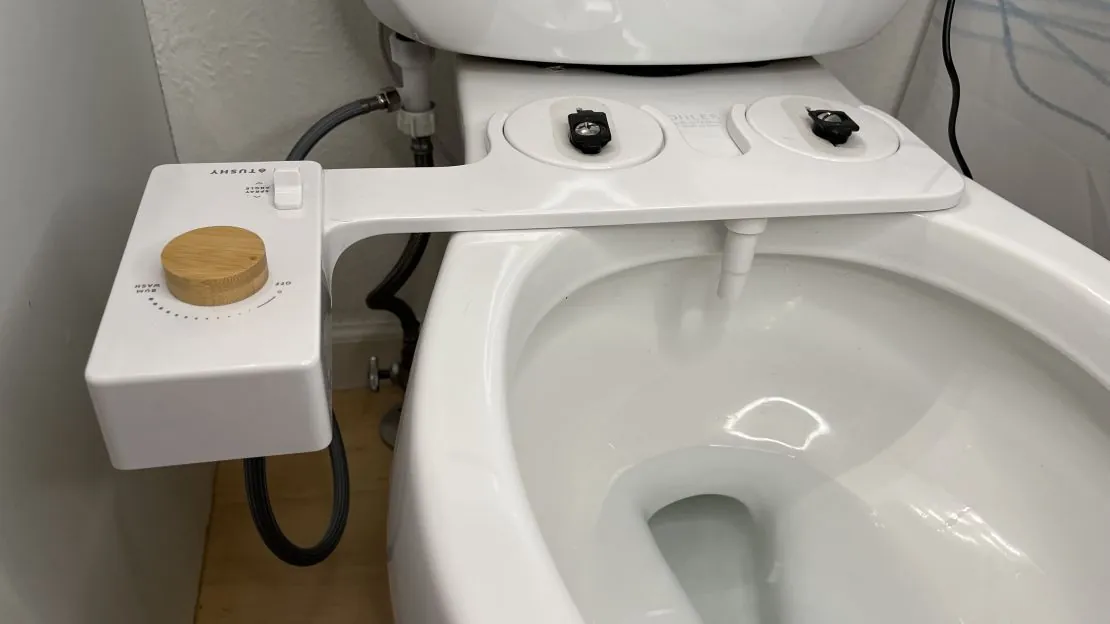 A sleek dual-nozzle bidet attachment displayed on a clean bathroom counter.