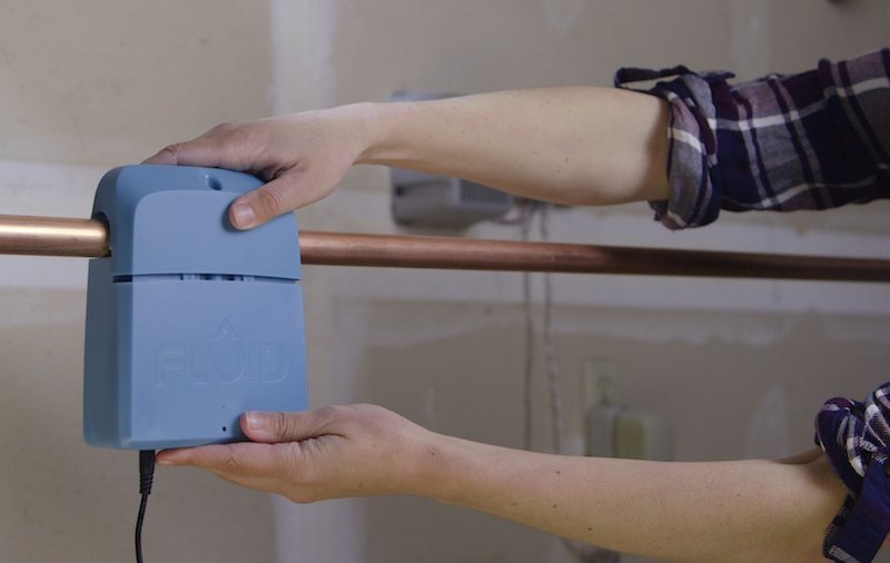 A smart water leak detector placed on a basement floor near a washing machine.