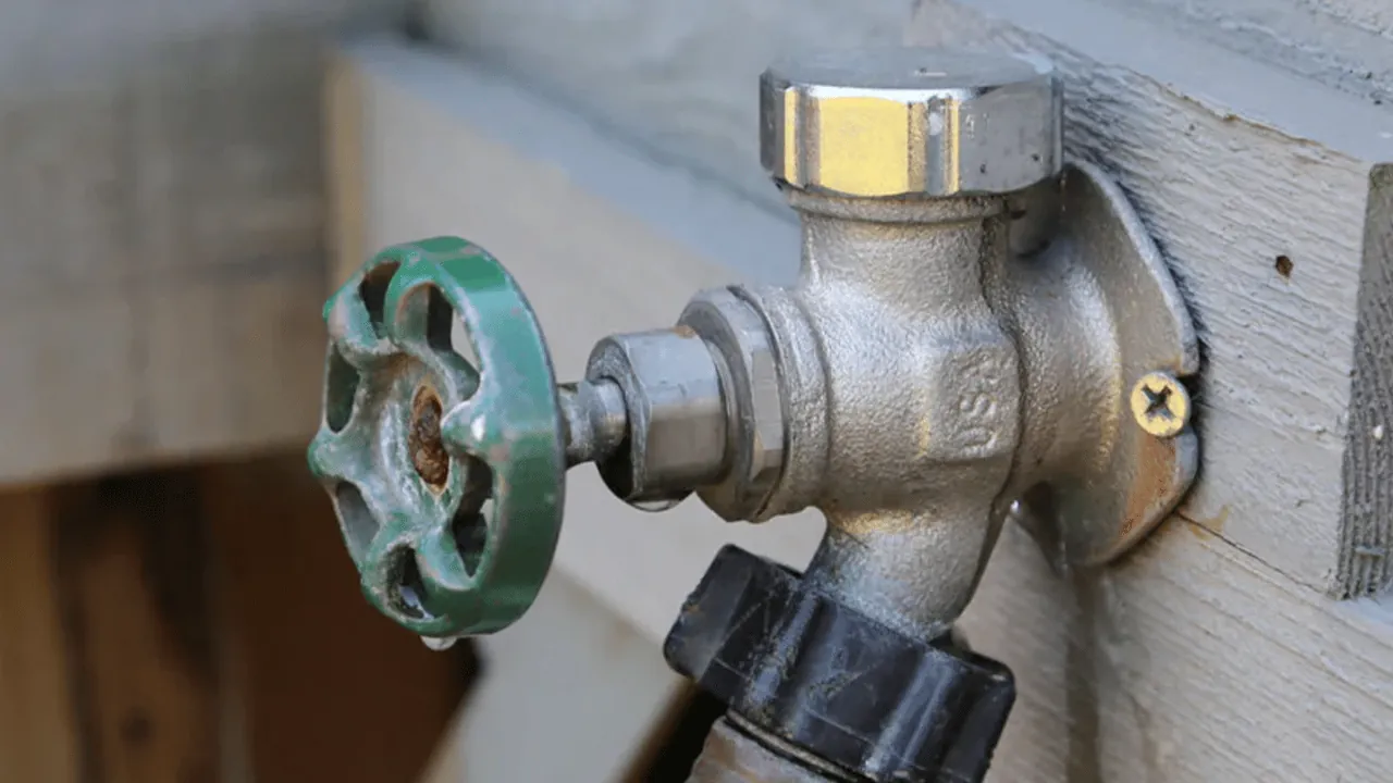 A standard compression outdoor faucet mounted directly onto a light beige house wall.