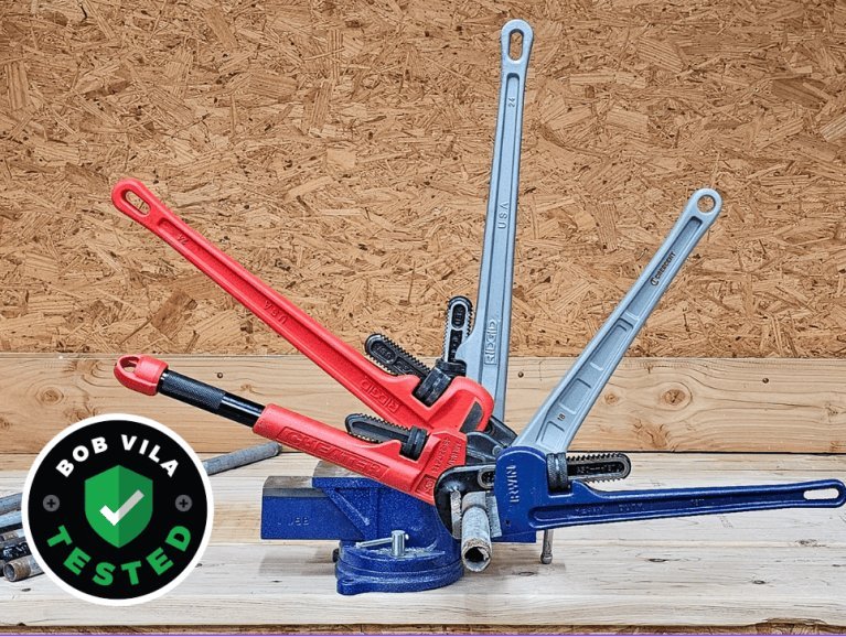 A variety of professional pipe wrenches displayed on a rustic wooden workshop bench.