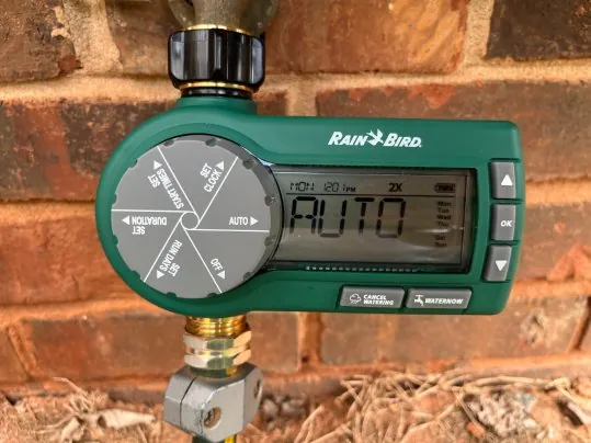 Various hose bib timers and batteries arranged on a wooden workbench.